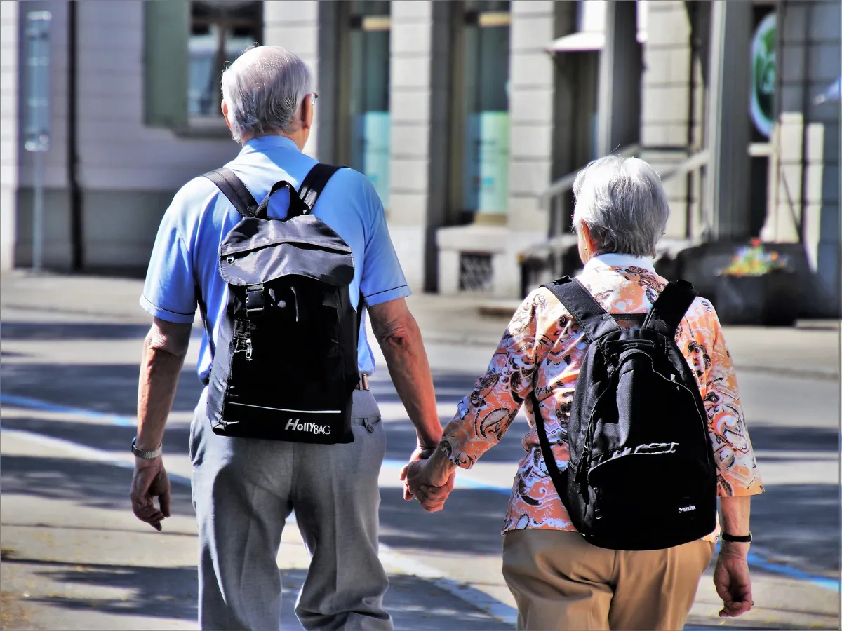 Casal de idosos de mãos dadas caminhando pela rua, vistos de costas