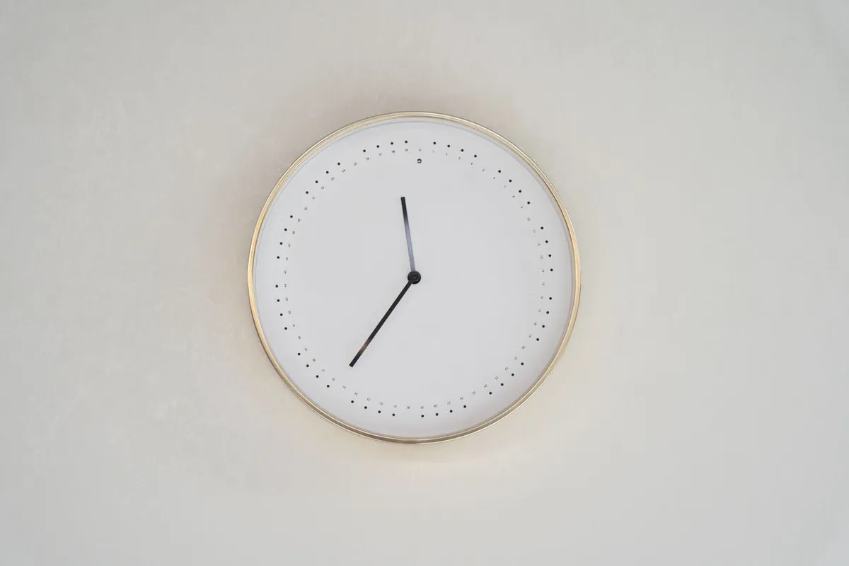 Relógio de parede minimalista de aro dourado em uma parede clara, marcando o passar das horas